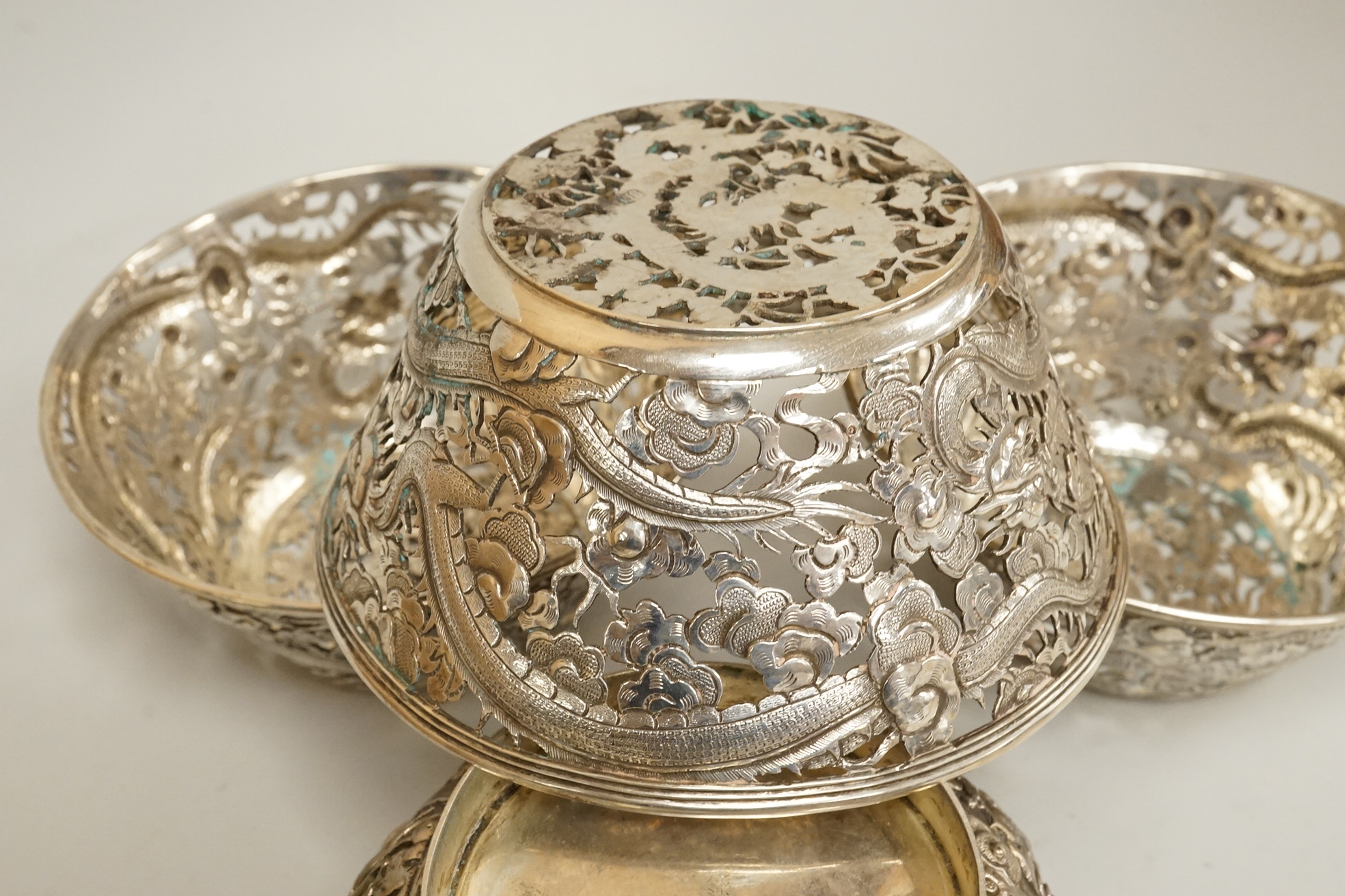 A set of three late 19th/early 20th century Chinese Export pierced white metal bowls, decorated with dragons, by Wang Hing, Hong Kong (lacking glass inserts?), diameter 12.5cm, together with one other similar Chinese Exp